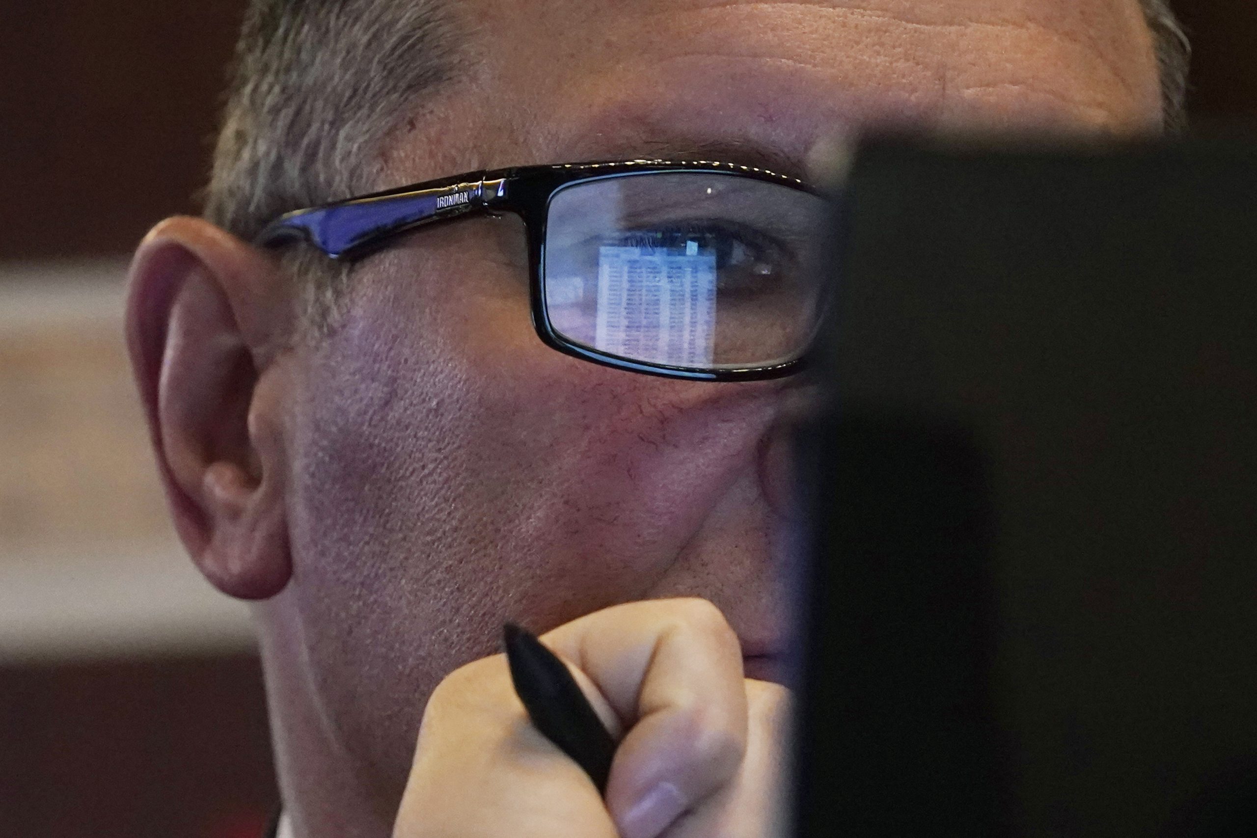 A trader’s handheld device is reflected in his glasses on...